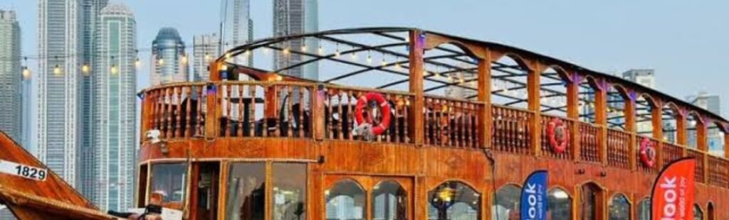 Traditional wooden dhow boat illuminated at night, sailing on Dubai's tranquil waters with the city skyline in the background.