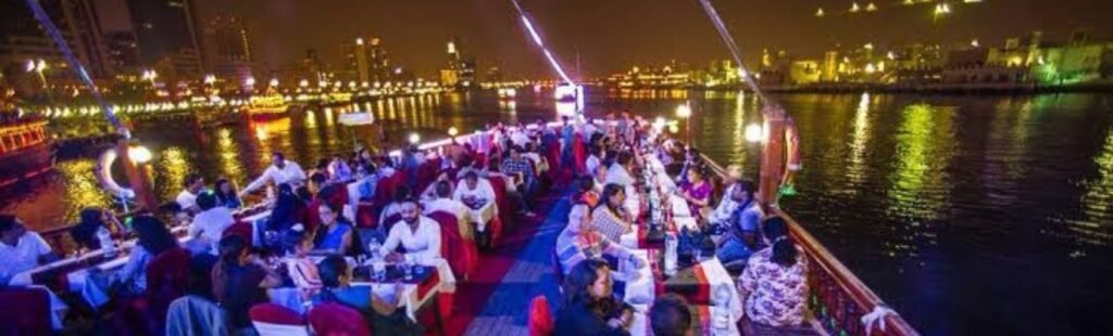 Dhow boat cruising under Dubai's illuminated skyline at night.