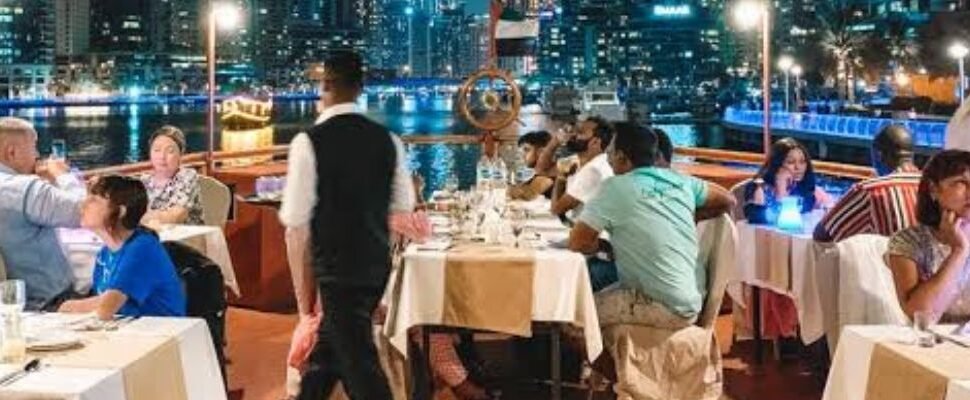 A luxurious dhow boat elegantly illuminated at night, cruising along Dubai's waters with the city skyline in the background.