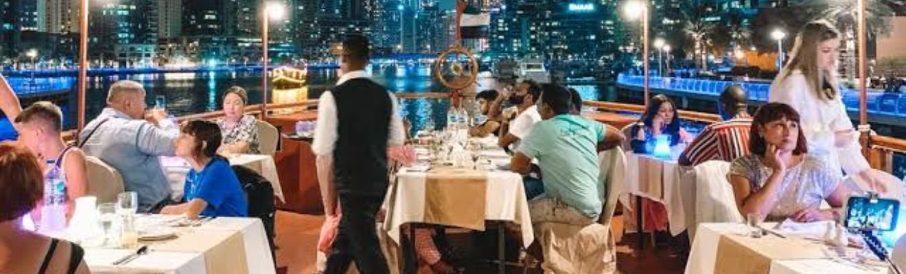 A luxurious dhow boat elegantly illuminated at night, cruising along Dubai's waters with the city skyline in the background.