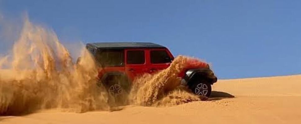 Vehicle driving over Dubai's sand dunes during sunset.