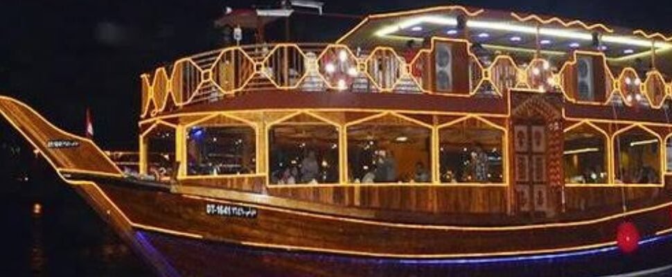 Traditional dhow boat sailing on Dubai Creek with city skyline.