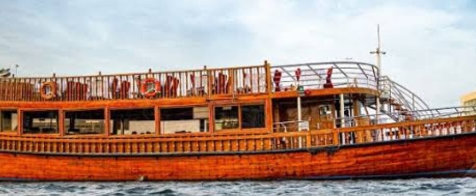 Traditional wooden dhow sailing in Dubai Marina at sunset.