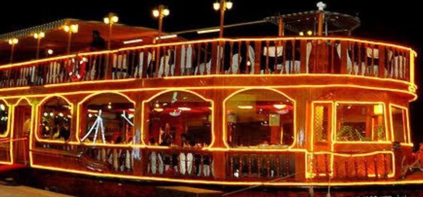 A luxury yacht cruising under the illuminated skyscrapers of Dubai Marina.