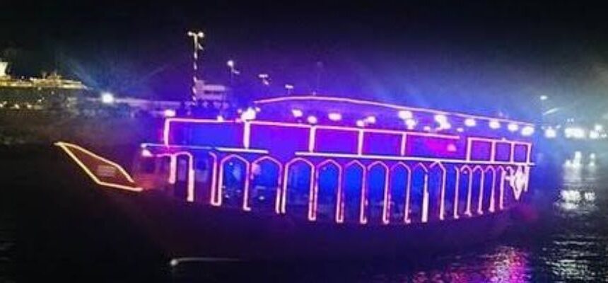 Traditional wooden dhow sailing along Dubai's waterfront at sunset.