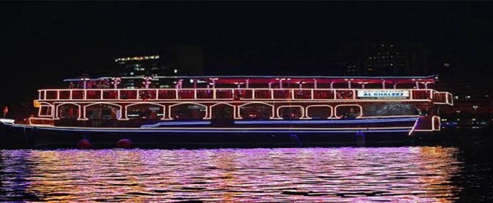 Traditional dhow boat cruising along Dubai Creek at twilight.