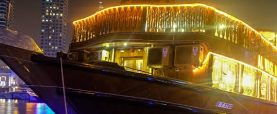 Traditional dhow boat cruising on Dubai Creek at sunset.