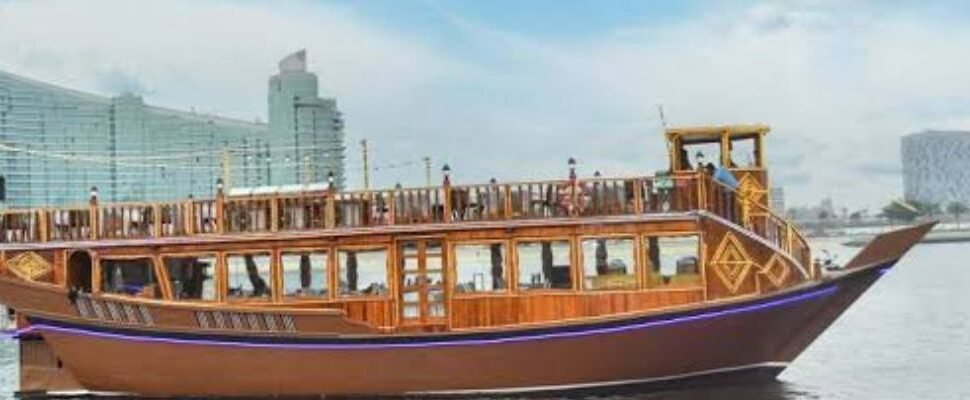 Traditional dhow boat cruising along Dubai Creek at sunset.