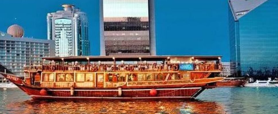 Traditional dhow boat cruising on Dubai Creek at sunset.