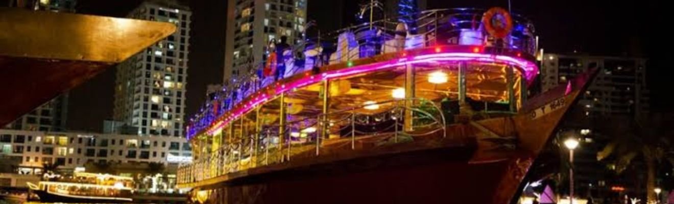 Traditional dhow boat cruising under Dubai Marina's night lights.