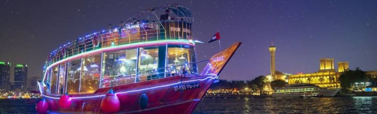 Dubai Marina lit up at night with a dhow cruise in the foreground.