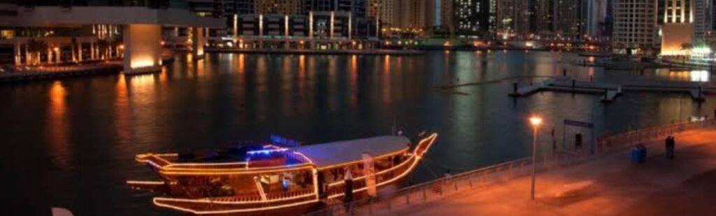 Nighttime view of Dubai Marina illuminated, with a cruise boat in the foreground.