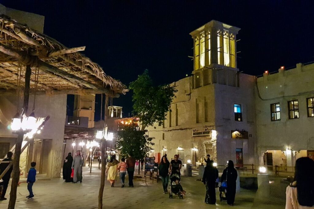 People strolling through a traditional-style Dubai night markets with old wind towers and lantern-lit pathways, enjoying the warm evening atmosphere.
