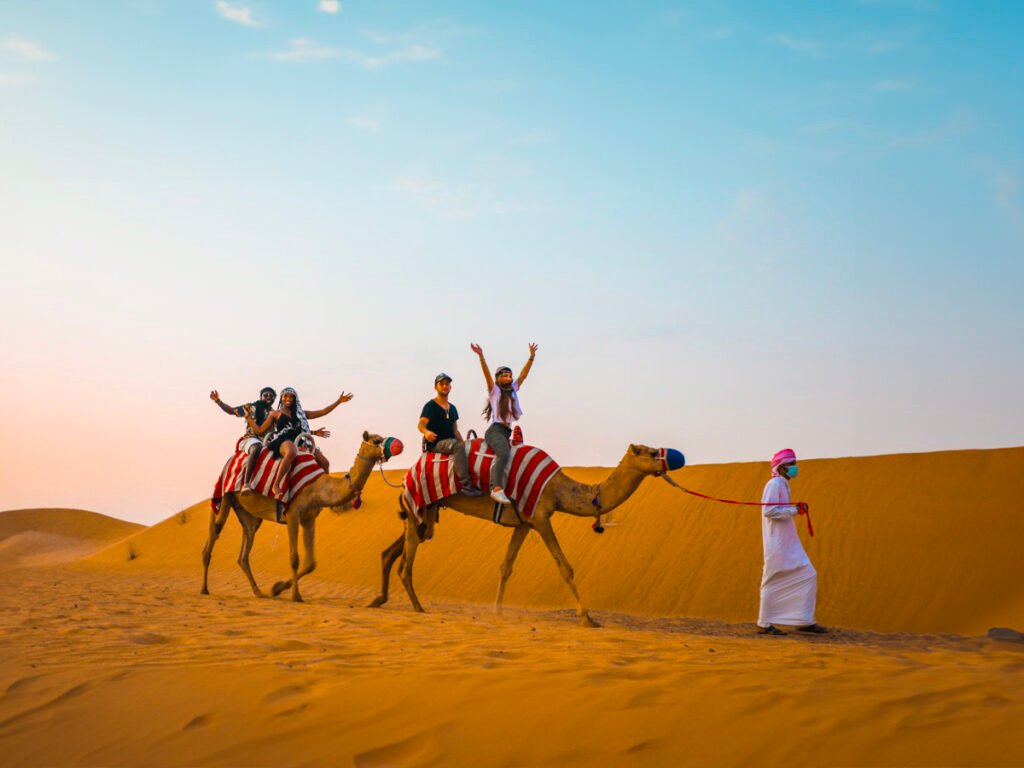 A stunning sunrise over the golden dunes during a Morning Desert Safari in Dubai, featuring a 4x4 vehicle, camel rides, and tourists enjoying the Dubai Morning Desert Safari experience.