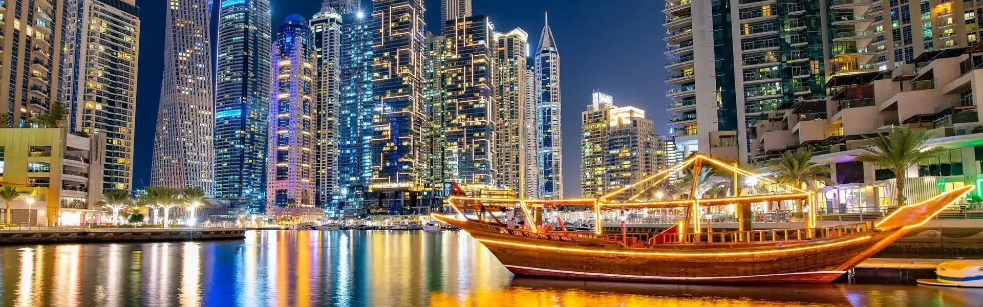 Traditional wooden boat lit up at night during a Dhow Cruise in Dubai, offering a luxurious Dhow Dinner Cruise experience at the Marina.