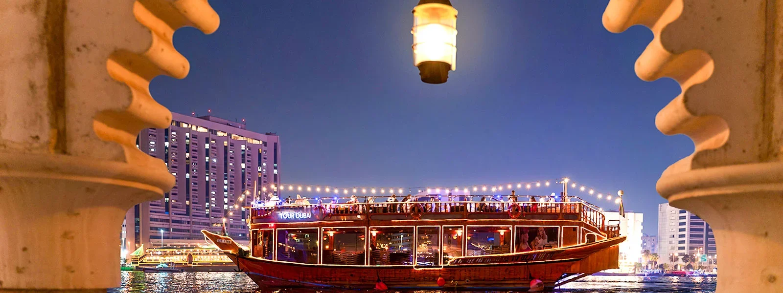 Traditional wooden dhow sailing on Dubai Marina during a Dhow cruise Dubai with guests enjoying a dinner cruise under city lights.