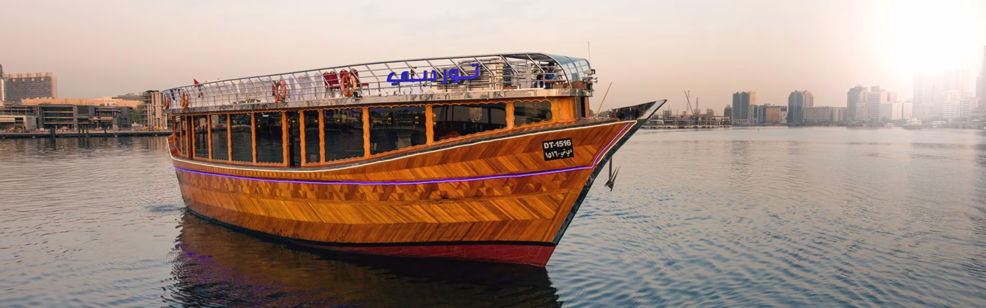 A scenic view of the Dubai Creek Dhow Cruise, showcasing the traditional dhow sailing along the vibrant waters of Dubai Creek, offering a unique creek cruise in Dubai.