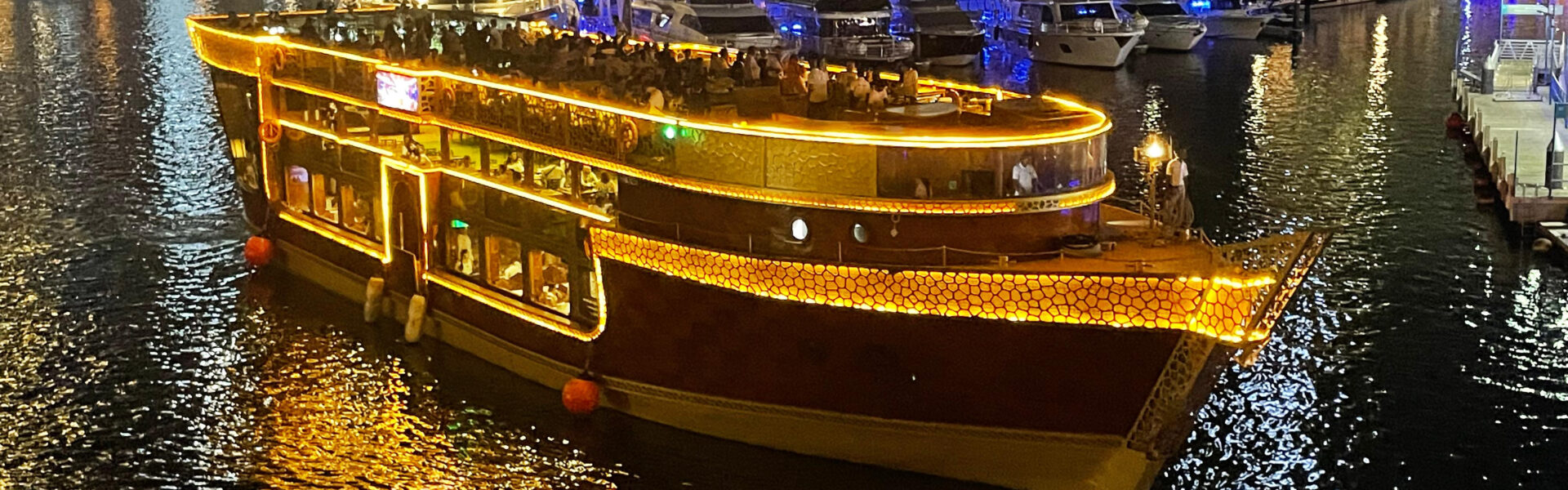 Traditional wooden boat lit up at night offering a marina dhow cruise with dinner, showcasing stunning skyline views during a cruise from Dubai.