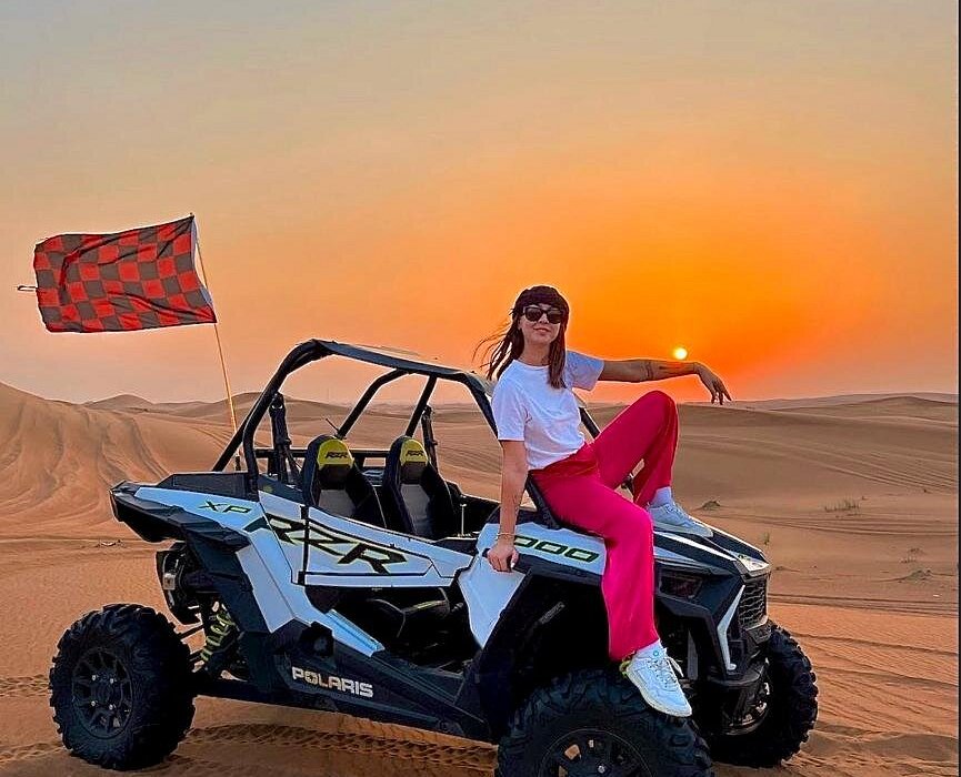 Sunset Adventure with Dune Buggy Dubai › Forever Tourism LLC Woman posing beside a dune buggy during a thrilling Dubai desert adventure at sunset.
