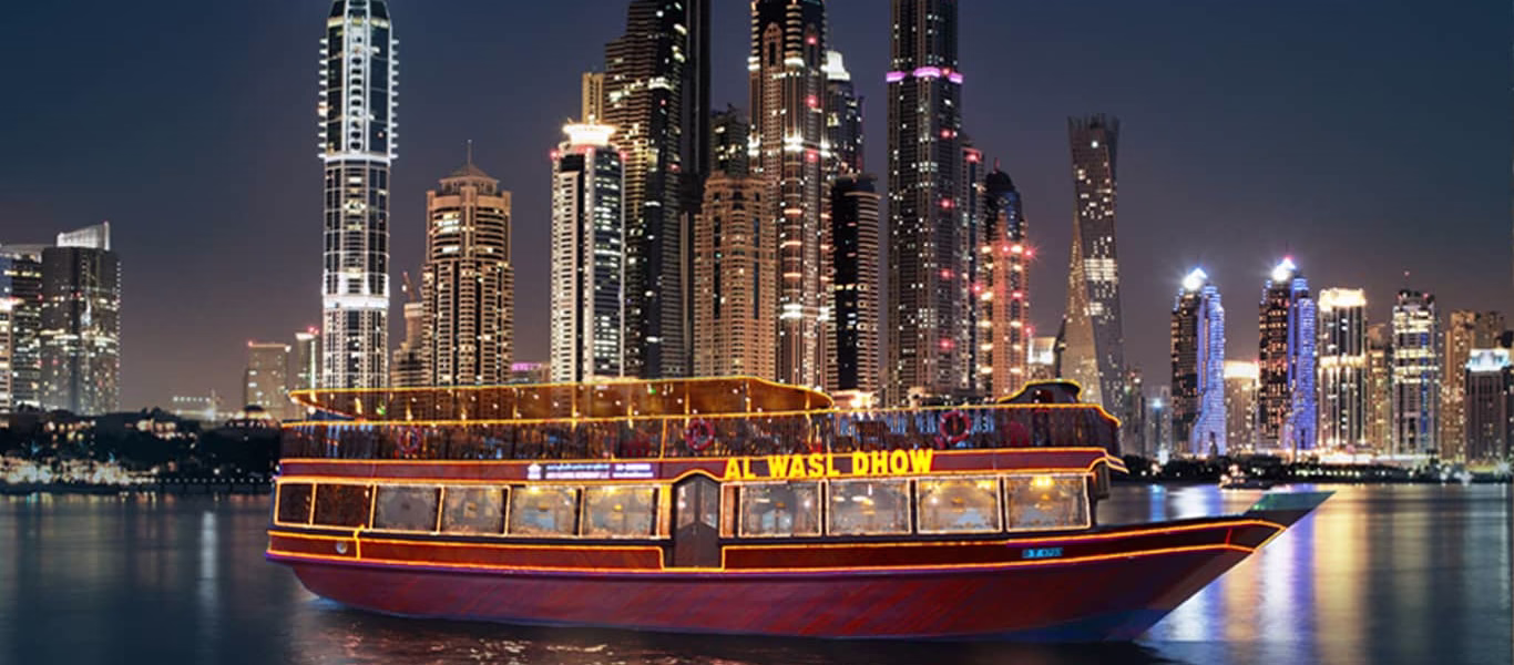 Traditional dhow sailing through Dubai Marina at night, lit up with lights, offering a Marina Dhow Cruise with Dinner experience.