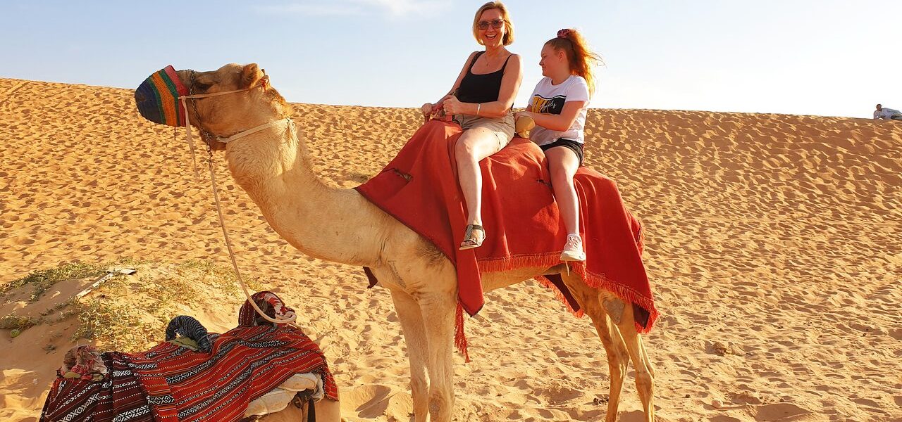 Tourists enjoying an evening desert safari Dubai with dune bashing, camel rides, and sunset over the golden sands of the Dubai desert safari.