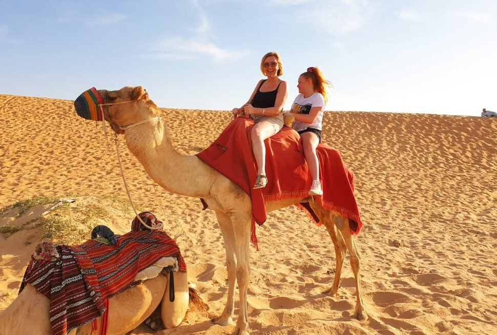 Tourists enjoying an evening desert safari Dubai with dune bashing, camel rides, and sunset over the golden sands of the Dubai desert safari.