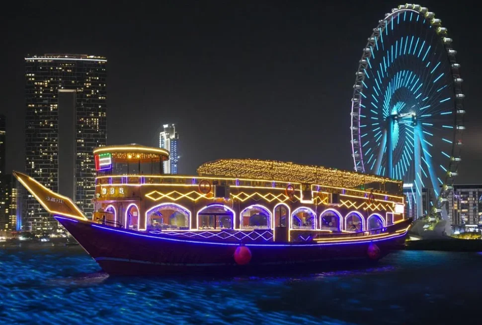 Traditional wooden dhow sailing through Dubai Marina at night, offering a Dhow Cruise in Dubai with dinner, city lights, and scenic waterfront views.