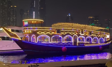 Guests enjoying a Marina dhow cruise with dinner on a beautifully lit traditional dhow boat against the Dubai Marina skyline.