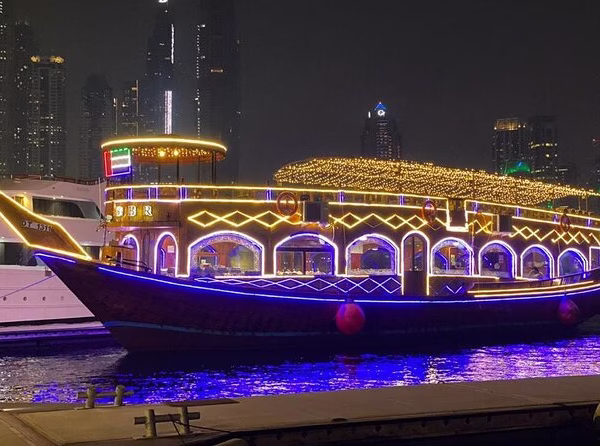 Guests enjoying a Marina dhow cruise with dinner on a beautifully lit traditional dhow boat against the Dubai Marina skyline.