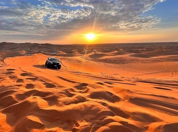 Tourists riding camels at sunset, capturing memorable Dubai desert safari photos during a scenic Desert Safari Dubai experience.