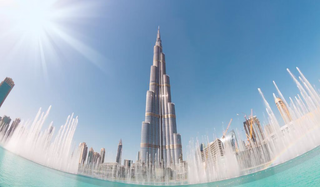 Night view of the Dubai Fountain performing with lights near Burj Khalifa, showcasing show times and visitor crowds.