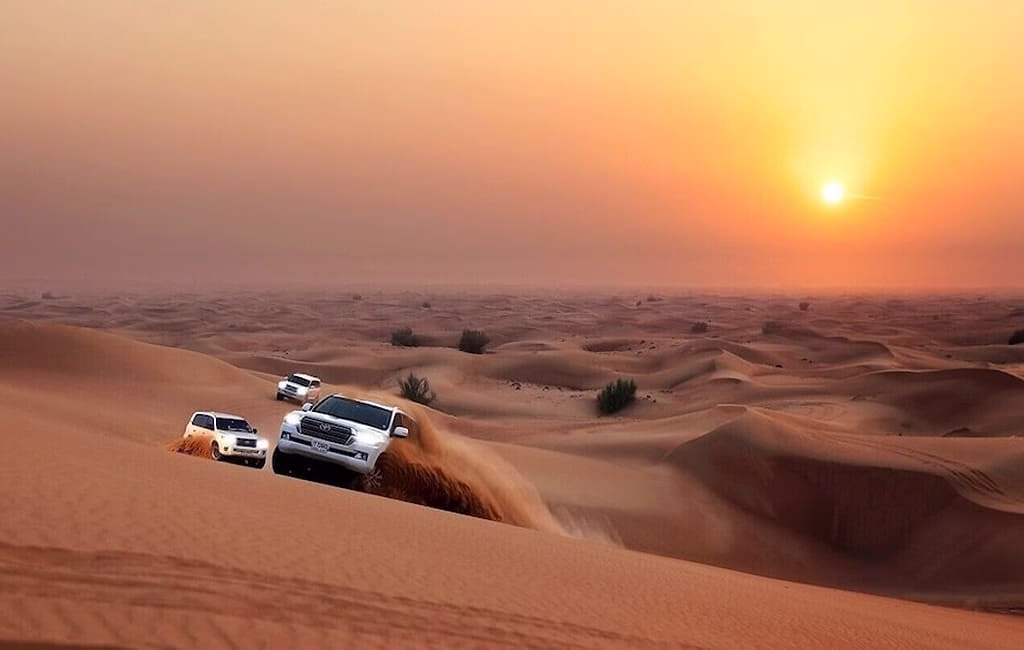 Tourists enjoying a sunrise desert safari Dubai at a scenic desert safari location with views of the golden sand dunes during early morning.