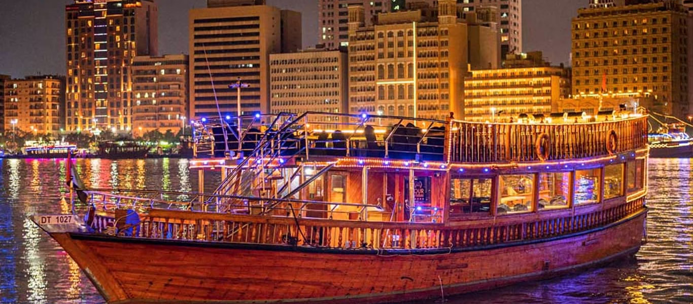 Traditional wooden dhow sailing on Dubai Creek at sunset during a creek dinner cruise with guests enjoying a dhow cruise dinner experience.