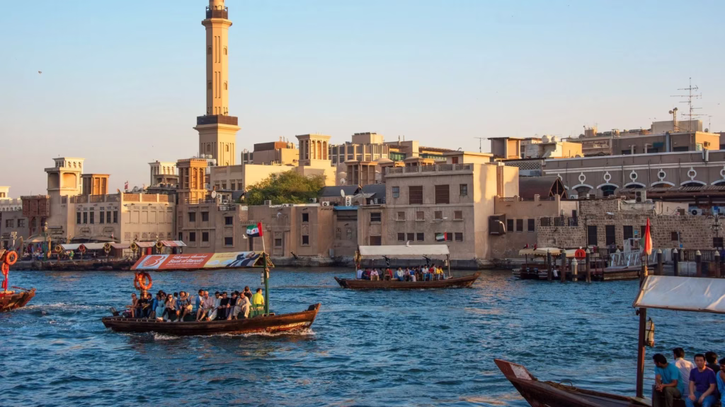 Traditional wooden dhow sailing on Dubai Creek at sunset during a creek dinner cruise with guests enjoying a dhow cruise dinner experience.