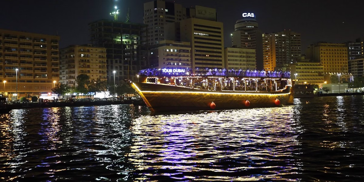 Traditional wooden boat sailing on Dubai Creek during a dhow cruise at Creek with dinner, lights, and guests enjoying the scenic Creek dinner cruise.