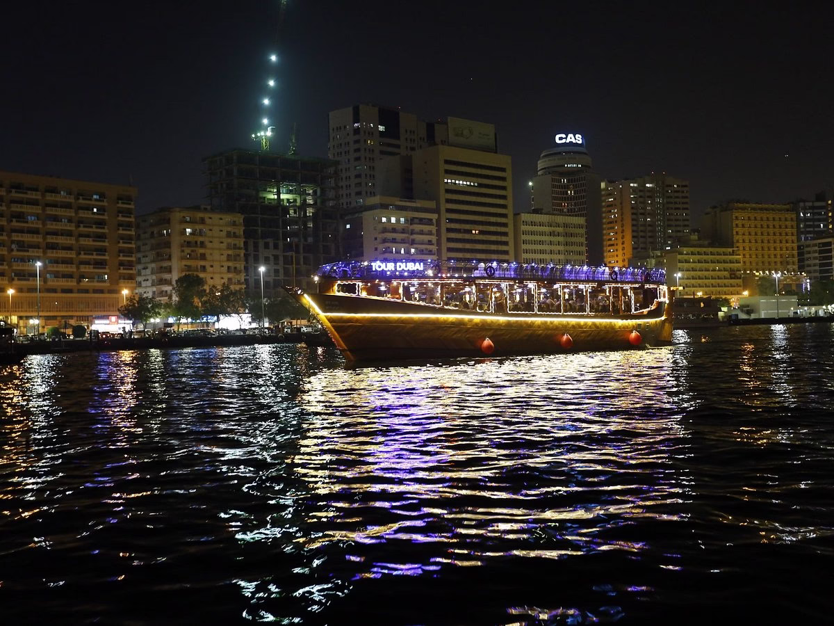 Traditional wooden boat sailing on Dubai Creek during a dhow cruise at Creek with dinner, lights, and guests enjoying the scenic Creek dinner cruise.
