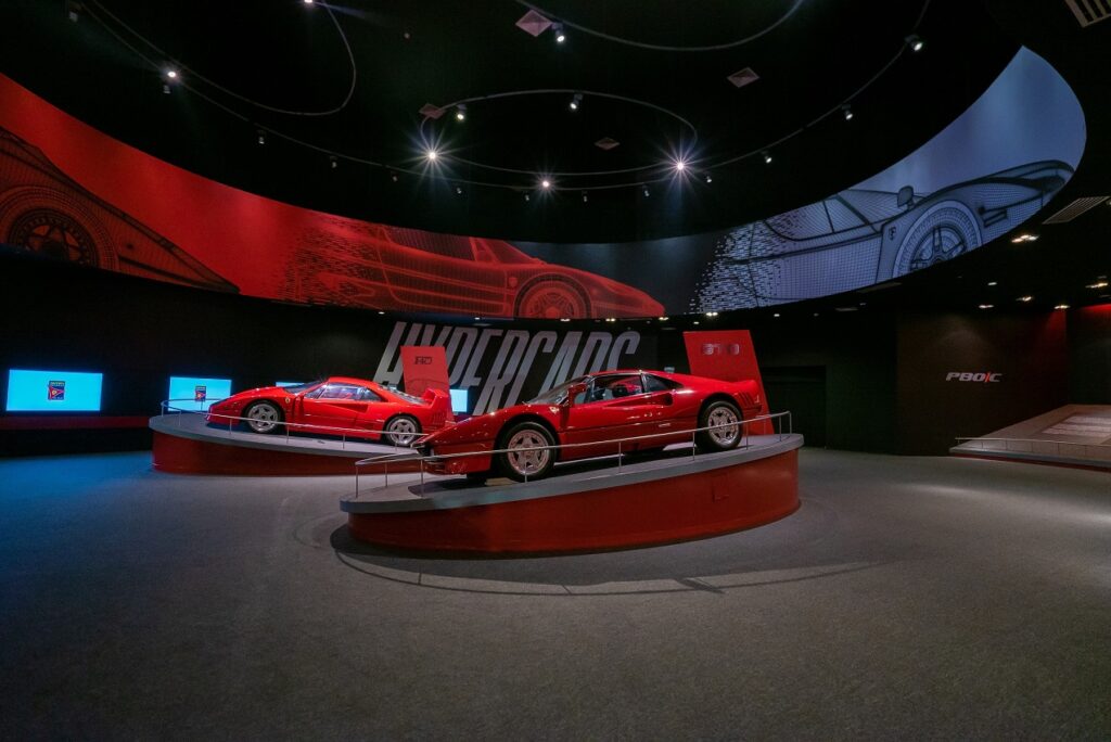 A couple poses in front of the iconic red roof of Ferrari World Abu Dhabi, holding their Ferrari World Abu Dhabi Tickets.
