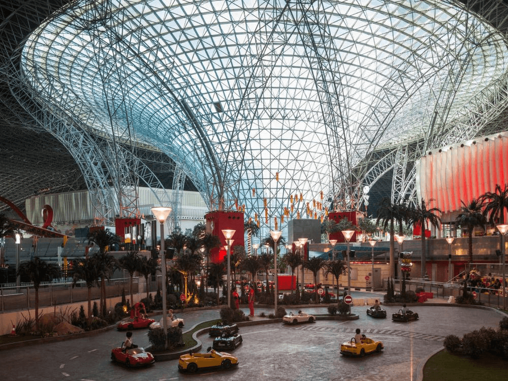 A couple poses in front of the iconic red roof of Ferrari World Abu Dhabi, holding their Ferrari World Abu Dhabi Tickets.