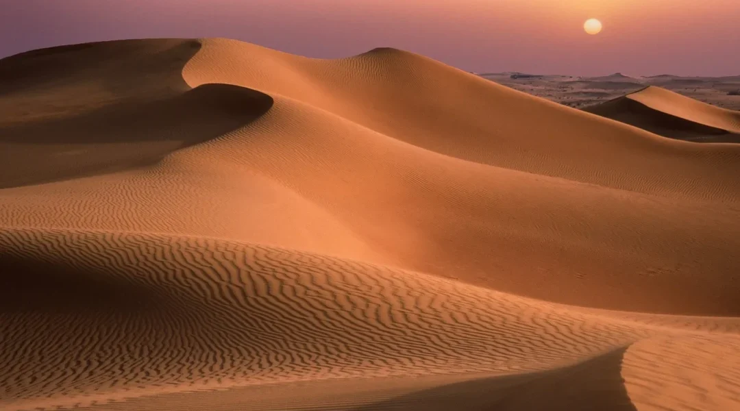 Vast golden Dubai Sand Dunes stretching into the horizon with clear blue skies, capturing the beauty of the Arabian desert landscape.