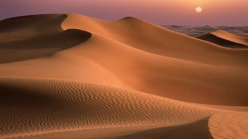 Traveler sand surfing down a red dune at sunset near Dubai