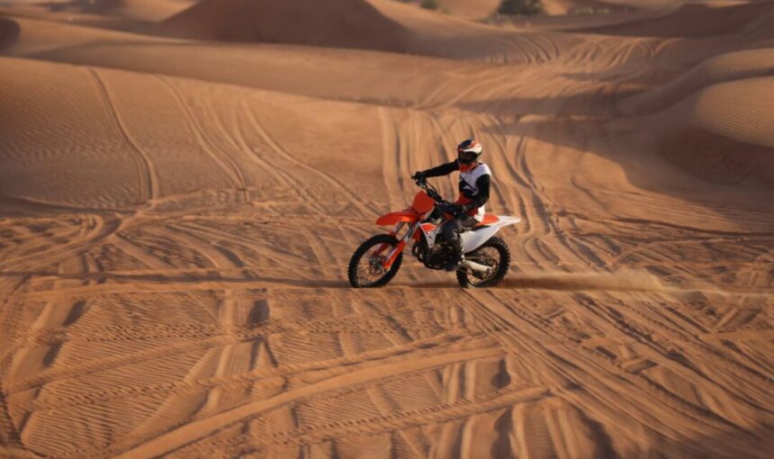 A rider on a red dirt bike speeding across golden desert dunes in Dubai during sunset.