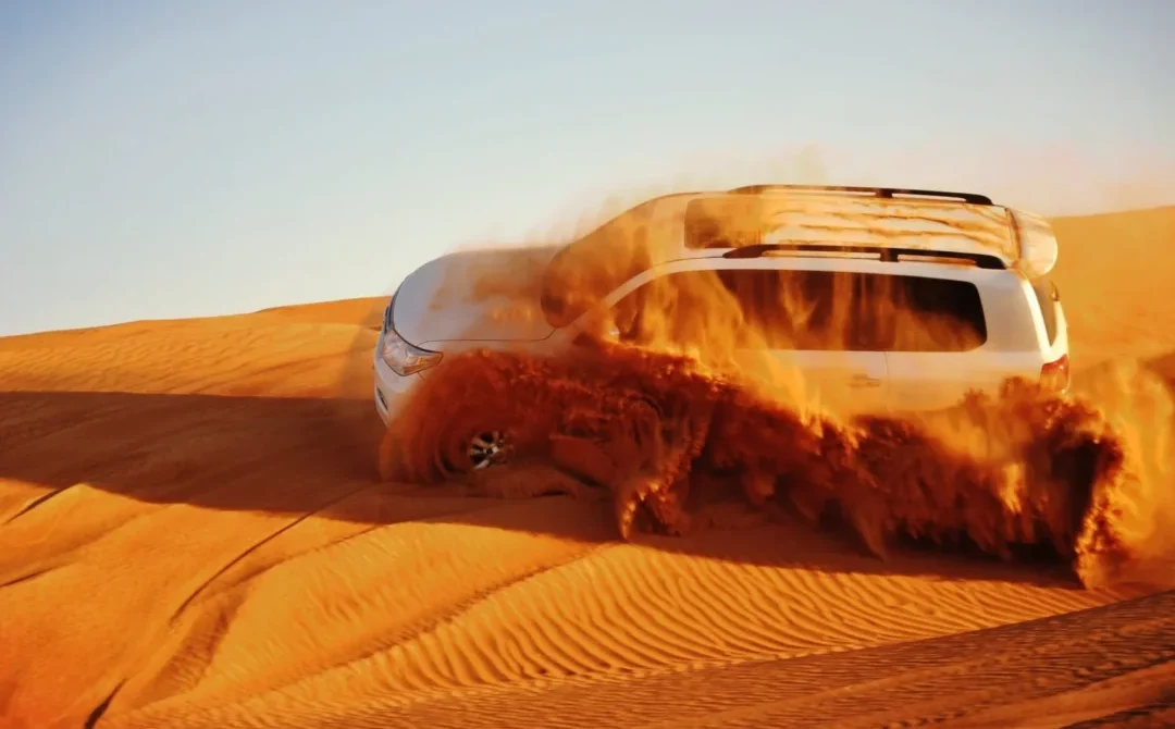 4x4 SUV kicks up a wave of red sand while dune bashing in the Dubai desert.