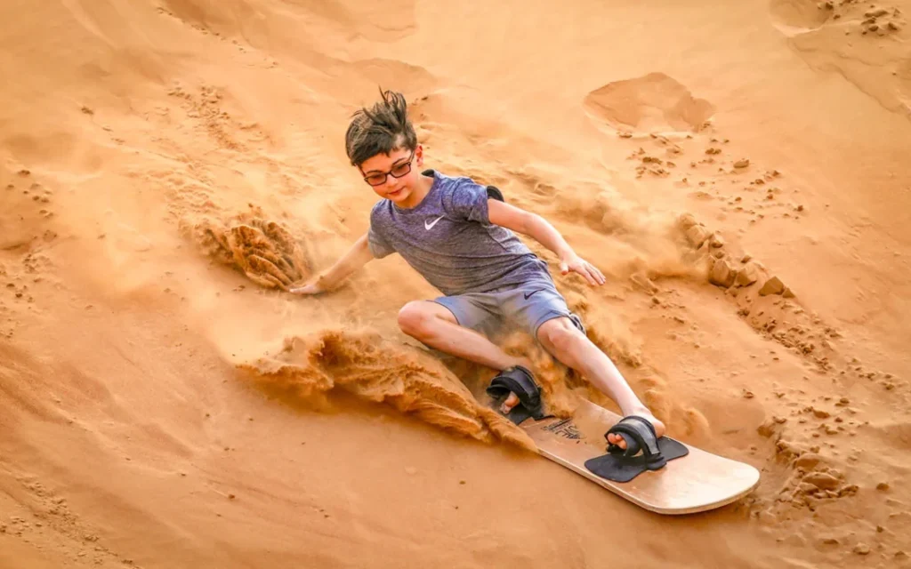 Traveler sand surfing down a red dune at sunset near Dubai
