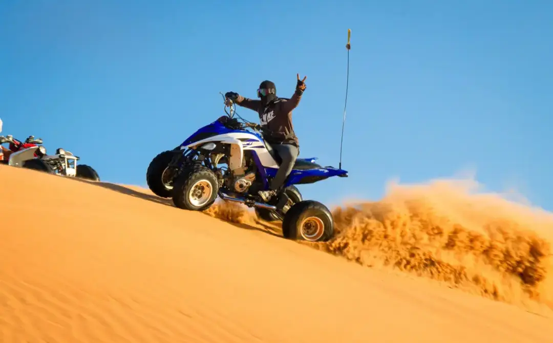 Rider on a blue quad bike speeding down golden sand dunes during a quad bike desert safari Dubai.