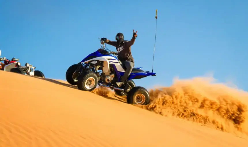 Quad Bike Desert Safari Dubai – Thrilling Adventure on the Golden Dunes › Forever Tourism LLC Rider on a blue quad bike speeding down golden sand dunes during a quad bike desert safari Dubai.
