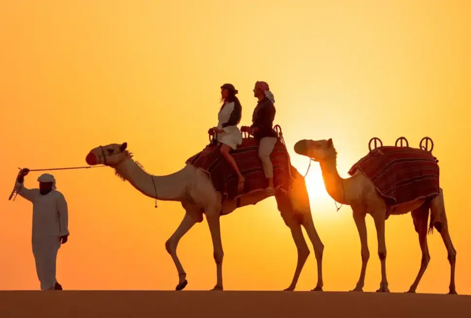 Arabian Safari on red dunes at sunset with 4×4, camel ride, and lantern-lit camp