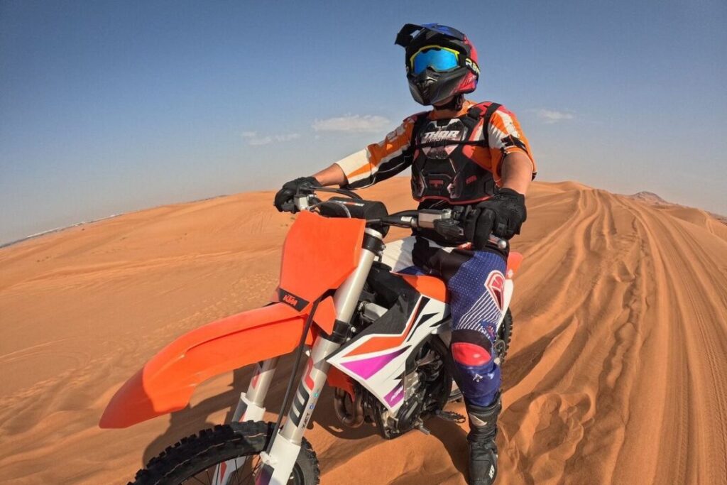 Dirt Bike Dubai - A dirt biker riding a KTM bike on the golden dunes of Dubai under a clear blue sky.