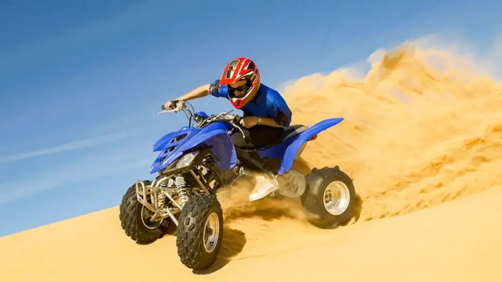 A person riding a blue quad bike across golden sand dunes during a desert safari Abu Dhabi.