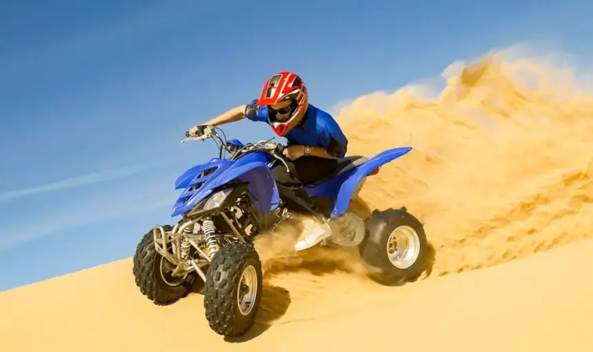 A person riding a blue quad bike across golden sand dunes during a desert safari Abu Dhabi.