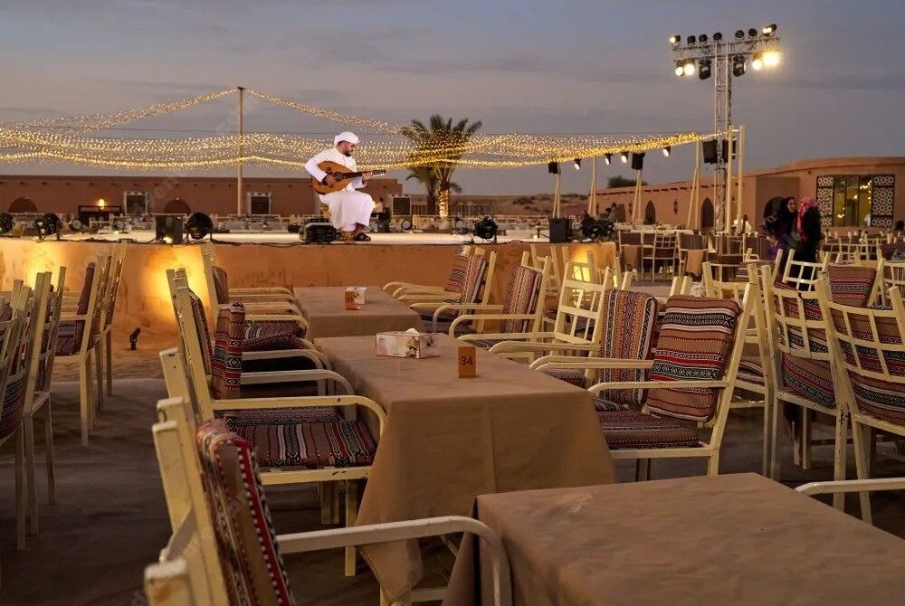 Evening Dining Experience at Lama Desert Safari Dubai › Forever Tourism LLC Outdoor dining setup with tables and stage for live performances at Lama Desert Safari Dubai during the evening desert experience.